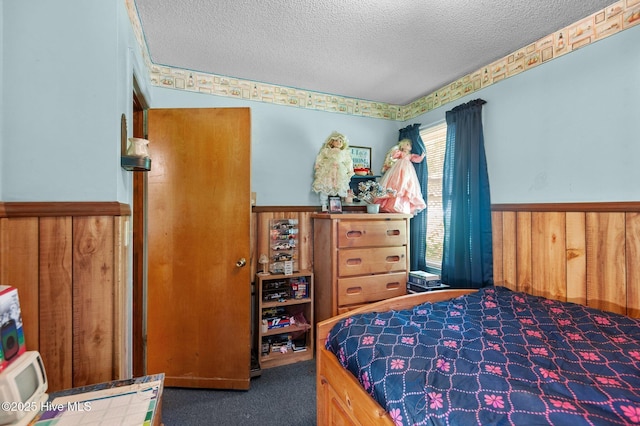 carpeted bedroom featuring wainscoting and a textured ceiling