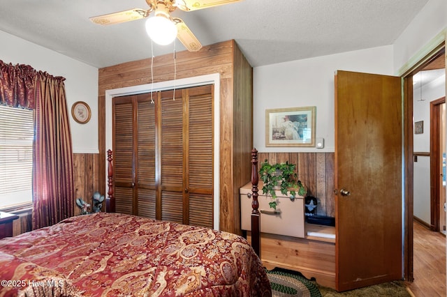 bedroom featuring wood walls, a closet, a wainscoted wall, wood finished floors, and a ceiling fan