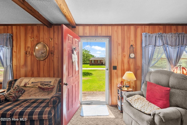 interior space featuring carpet flooring, access to exterior, beam ceiling, a textured ceiling, and wooden walls