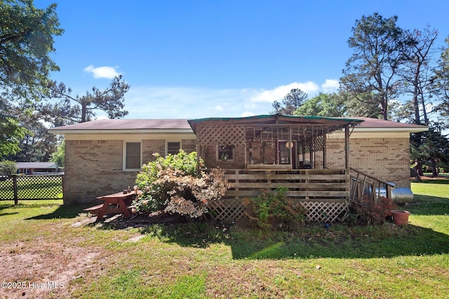 rear view of property featuring a lawn, a wooden deck, brick siding, and fence