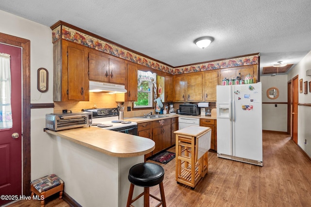 kitchen with a textured ceiling, under cabinet range hood, white appliances, light wood-style floors, and light countertops