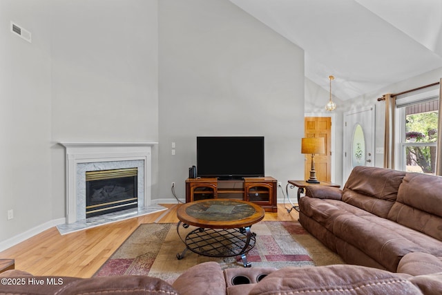 living room featuring wood finished floors, visible vents, a premium fireplace, baseboards, and high vaulted ceiling