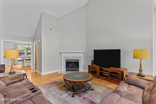 living room featuring high vaulted ceiling, an inviting chandelier, light wood-style flooring, baseboards, and visible vents