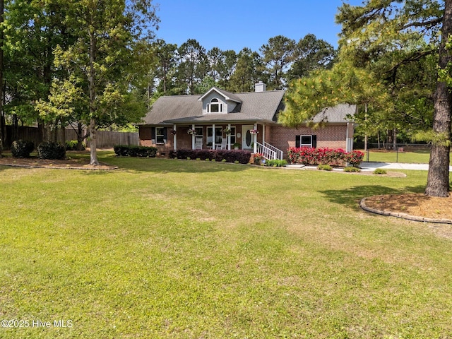 cape cod home with a front lawn, a porch, a chimney, fence, and brick siding
