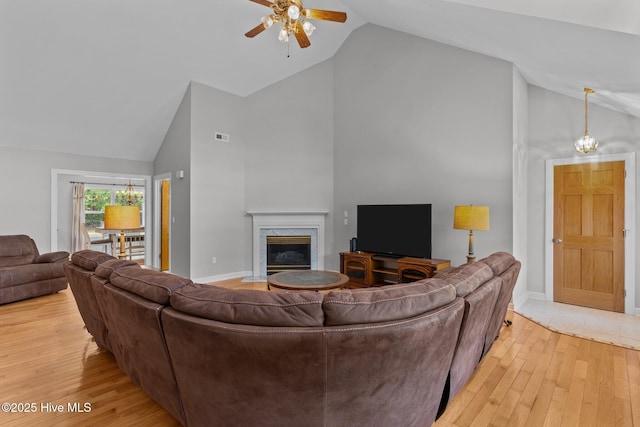living area with high vaulted ceiling, a fireplace, a ceiling fan, and light wood-type flooring