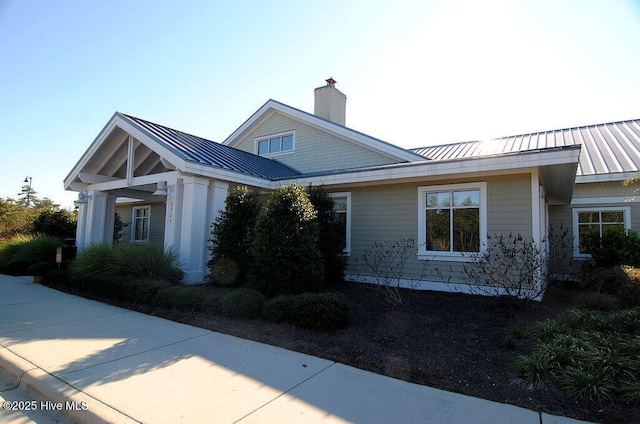 view of side of property with a standing seam roof, a chimney, and metal roof