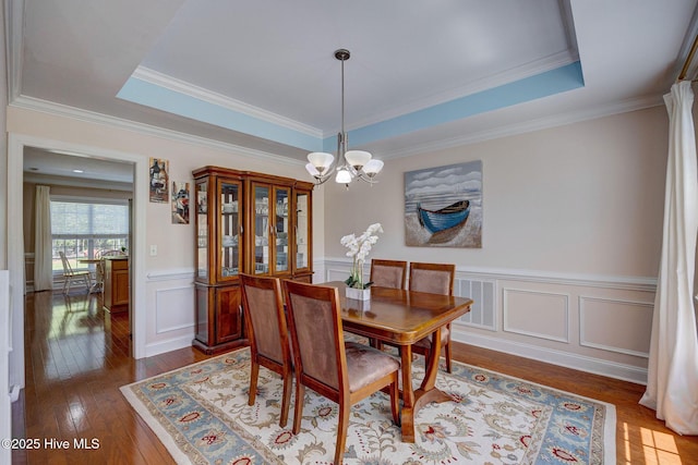 dining area featuring dark wood-type flooring, a raised ceiling, a wainscoted wall, and a chandelier