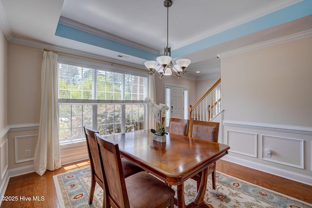 dining room featuring light wood-style floors, wainscoting, a decorative wall, and a notable chandelier