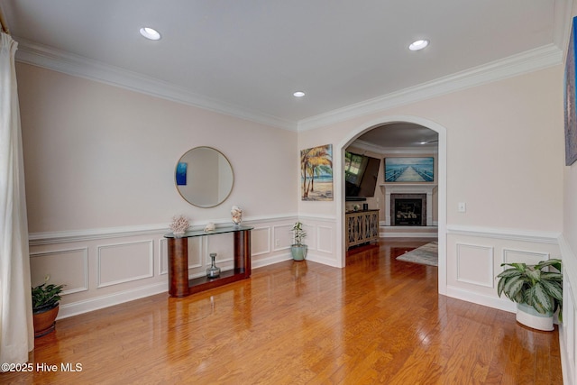 interior space featuring arched walkways, a wainscoted wall, a fireplace with raised hearth, ornamental molding, and a decorative wall