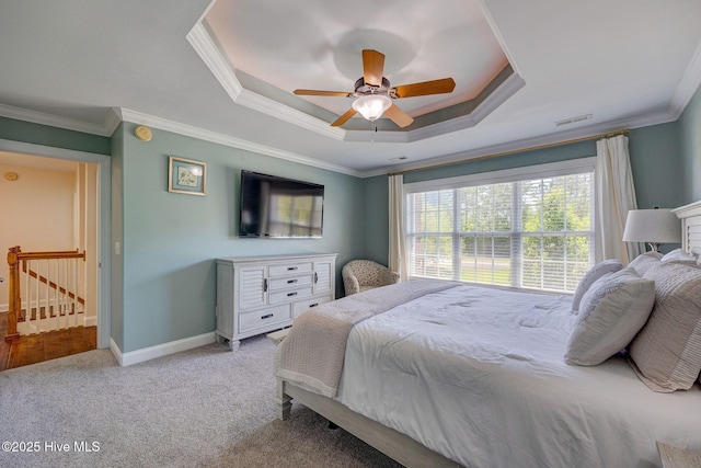 carpeted bedroom featuring ceiling fan, visible vents, baseboards, ornamental molding, and a tray ceiling