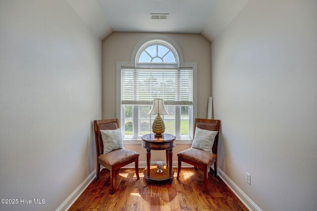 living area with baseboards, lofted ceiling, wood finished floors, and visible vents