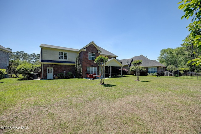 rear view of property featuring fence, a sunroom, a yard, and brick siding