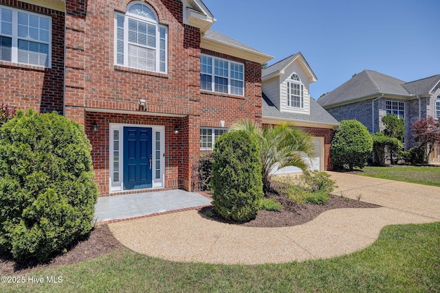 view of exterior entry with a garage, a shingled roof, concrete driveway, and brick siding