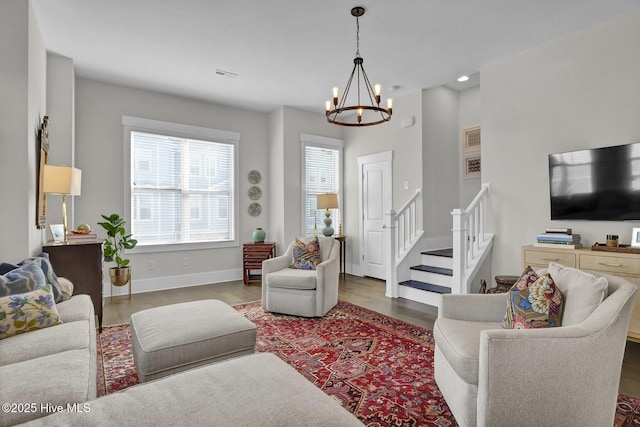 living room featuring an inviting chandelier, visible vents, wood finished floors, baseboards, and stairway