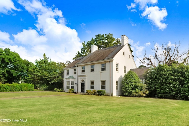colonial house featuring a chimney, stucco siding, and a front lawn