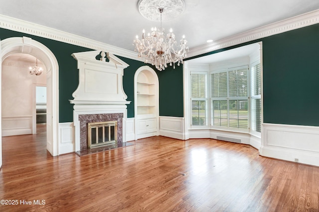 unfurnished living room featuring an inviting chandelier, ornamental molding, visible vents, and built in shelves