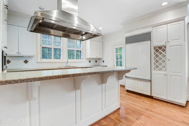 kitchen featuring crown molding, paneled built in refrigerator, island range hood, and a sink