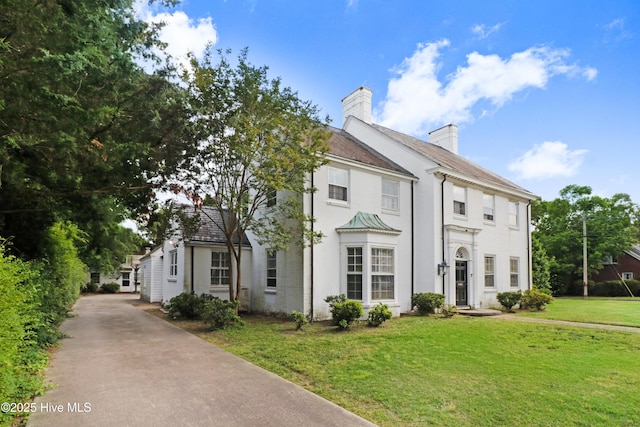 view of front facade with a chimney, driveway, stucco siding, and a front lawn