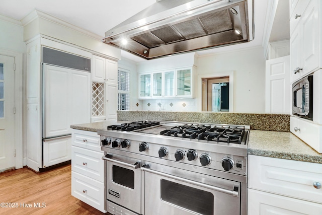 kitchen with wall chimney exhaust hood, light wood-style flooring, high quality appliances, glass insert cabinets, and white cabinets