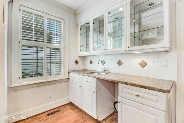 bar featuring light wood finished floors, visible vents, a sink, crown molding, and tasteful backsplash