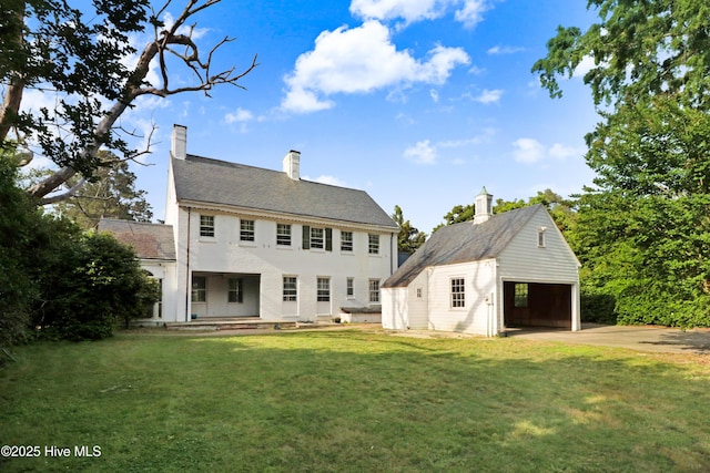 rear view of house with a yard, a chimney, an outdoor structure, and driveway
