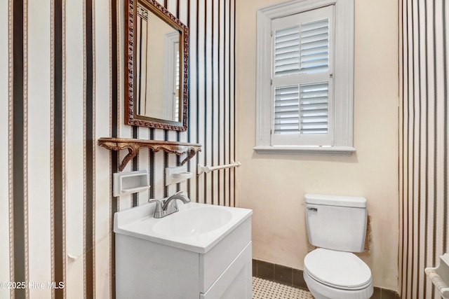 half bathroom with vanity, toilet, wallpapered walls, and tile patterned flooring