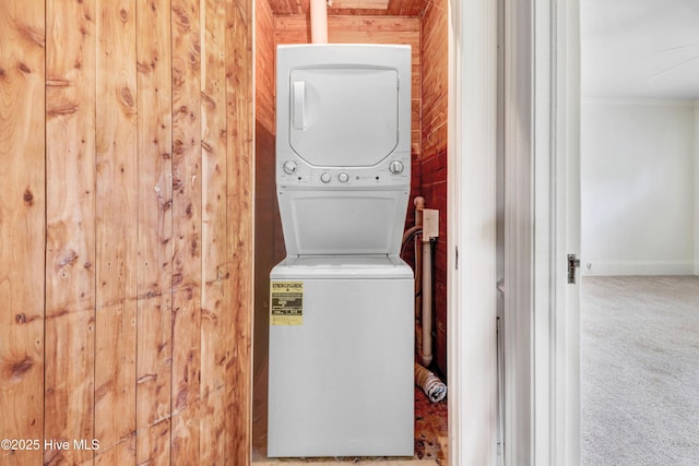 clothes washing area featuring stacked washer and dryer, laundry area, crown molding, and carpet