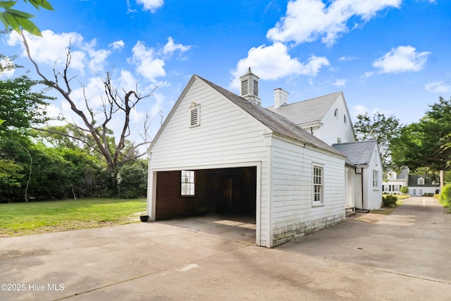 view of side of home featuring a garage, a chimney, a lawn, a shingled roof, and concrete driveway