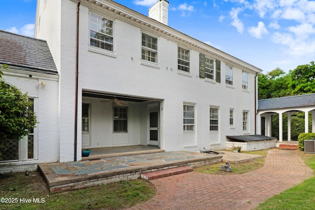 back of house with a chimney, a patio area, brick siding, and central air condition unit