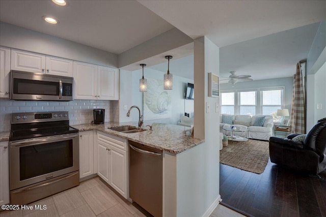 kitchen with stainless steel appliances, a sink, light stone countertops, open floor plan, and white cabinetry