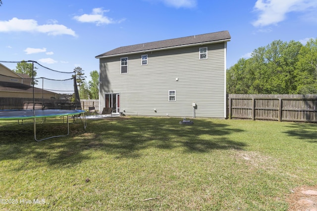 rear view of house with a trampoline, a lawn, and a fenced backyard
