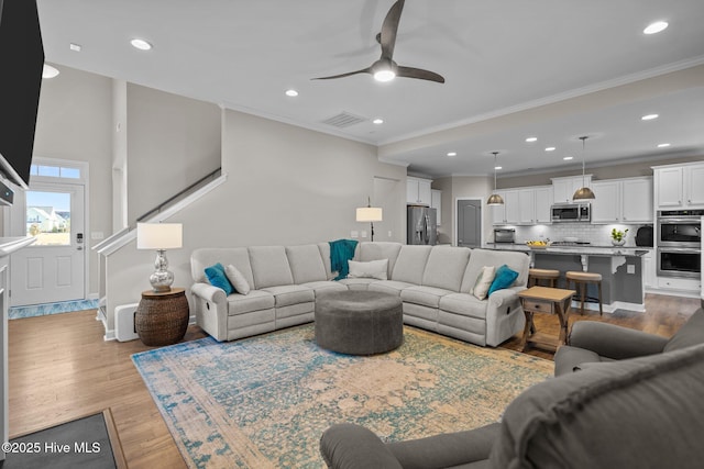 living area featuring ceiling fan, ornamental molding, wood finished floors, recessed lighting, and stairs