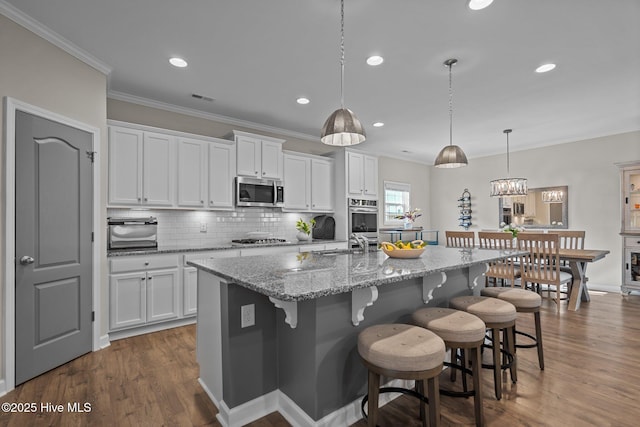 kitchen featuring stainless steel appliances, crown molding, white cabinetry, a sink, and a breakfast bar area