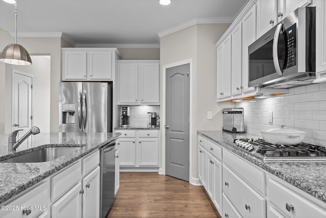 kitchen with stainless steel appliances, a sink, white cabinets, decorative backsplash, and ornamental molding