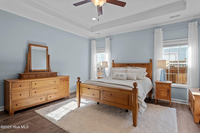bedroom with a tray ceiling, wood finished floors, crown molding, ceiling fan, and baseboards