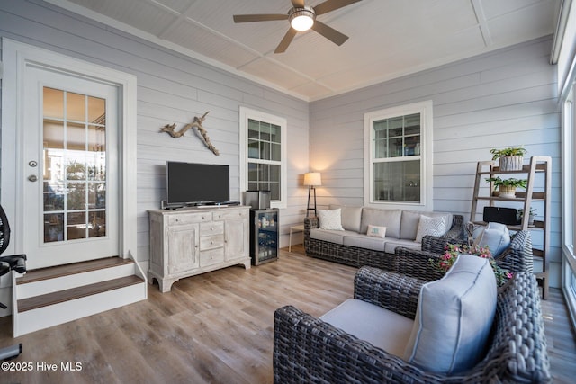 living area with a ceiling fan, wood walls, wood finished floors, and beverage cooler