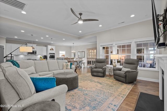 living room featuring a ceiling fan, ornamental molding, recessed lighting, wood finished floors, and a fireplace with flush hearth