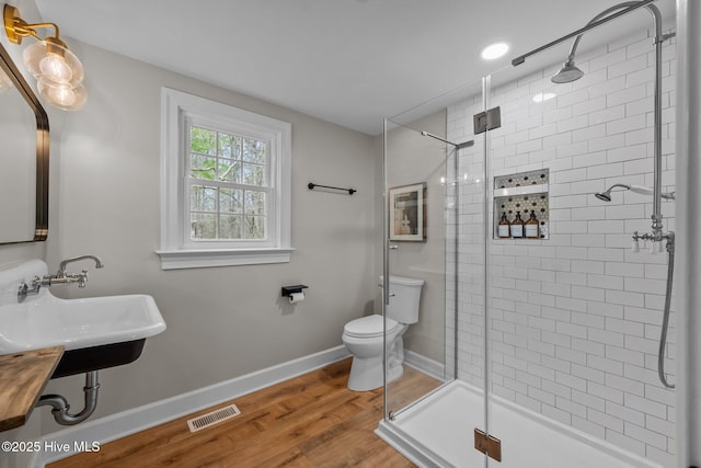 full bathroom featuring visible vents, wood finished floors, toilet, a shower stall, and a sink