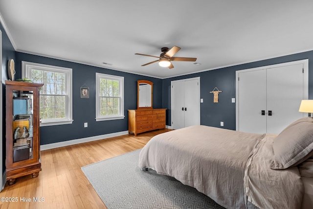 bedroom with light wood-style floors, two closets, a ceiling fan, baseboards, and ornamental molding