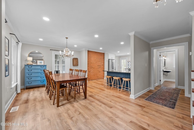 dining area featuring visible vents, crown molding, arched walkways, light wood-type flooring, and an inviting chandelier