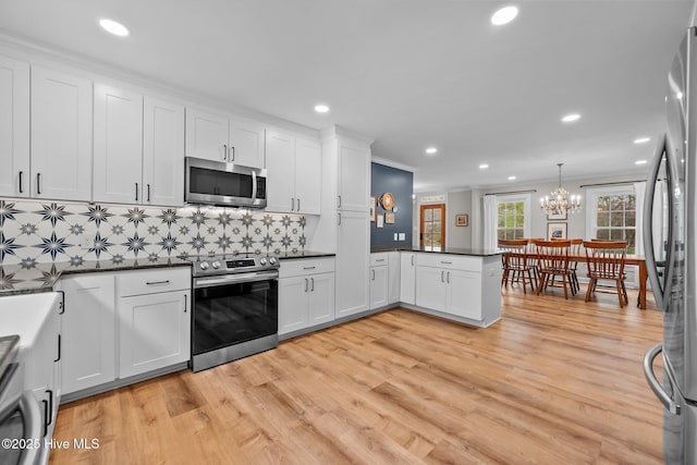 kitchen with white cabinets, dark countertops, light wood-style floors, stainless steel appliances, and a peninsula