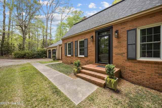 view of exterior entry with a yard, brick siding, and roof with shingles