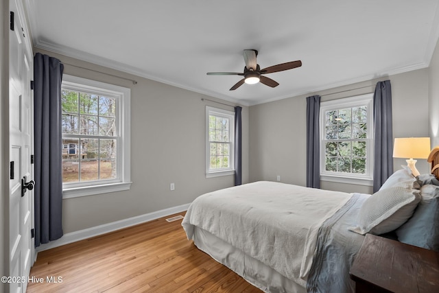 bedroom with baseboards, ornamental molding, multiple windows, and light wood-type flooring