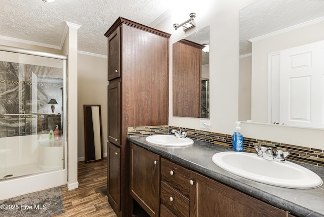 full bath with a textured ceiling, a shower stall, ornamental molding, and a sink