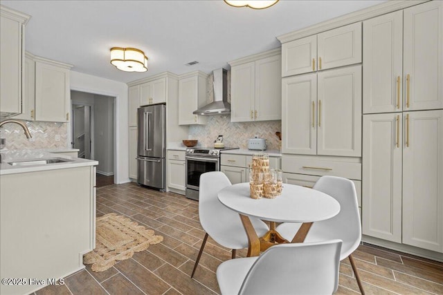 kitchen featuring appliances with stainless steel finishes, wall chimney exhaust hood, a sink, backsplash, and light countertops