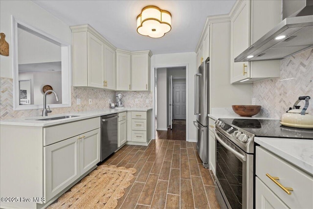 kitchen featuring stainless steel appliances, a sink, wall chimney exhaust hood, backsplash, and light countertops