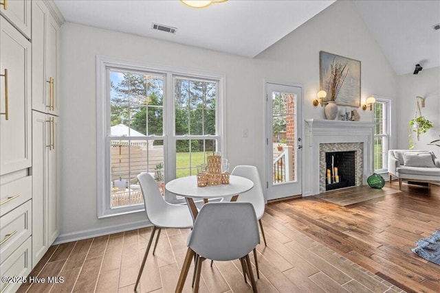 dining space with light wood-style floors, healthy amount of natural light, a fireplace with flush hearth, lofted ceiling, and baseboards