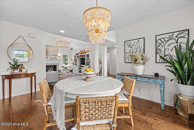 dining room with a chandelier, wood finished floors, a warm lit fireplace, baseboards, and recessed lighting
