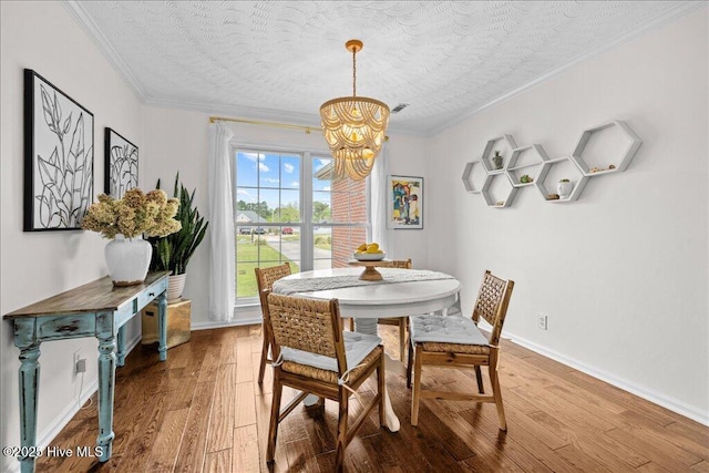 dining area featuring a chandelier, crown molding, wood-type flooring, a textured ceiling, and baseboards