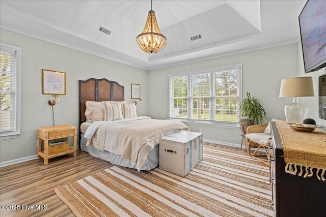 bedroom featuring a chandelier, light wood-style flooring, baseboards, a raised ceiling, and crown molding